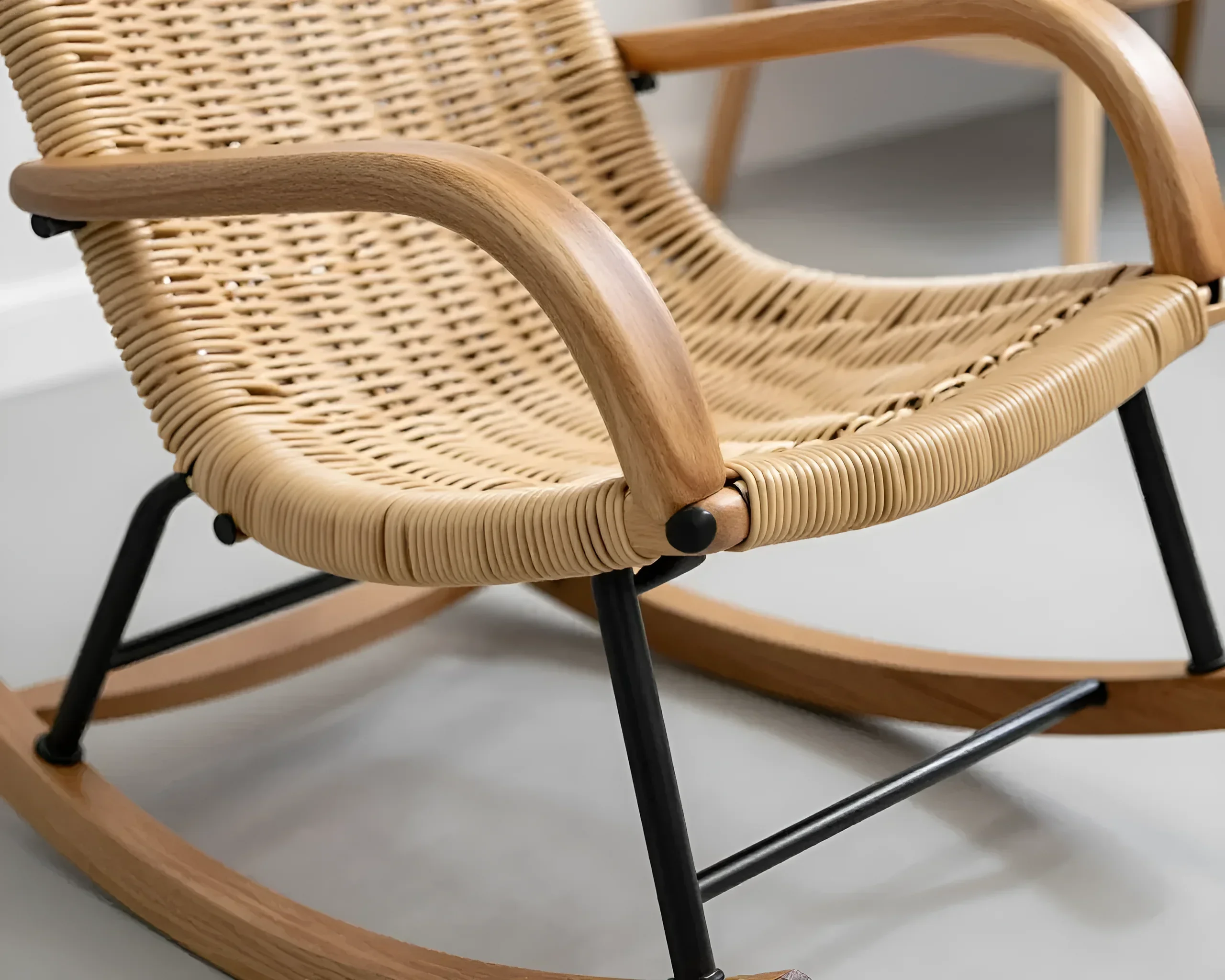 Close-up of a woven seat and back of a rocking chair with wooden armrests and metal legs, showing texture and natural materials.