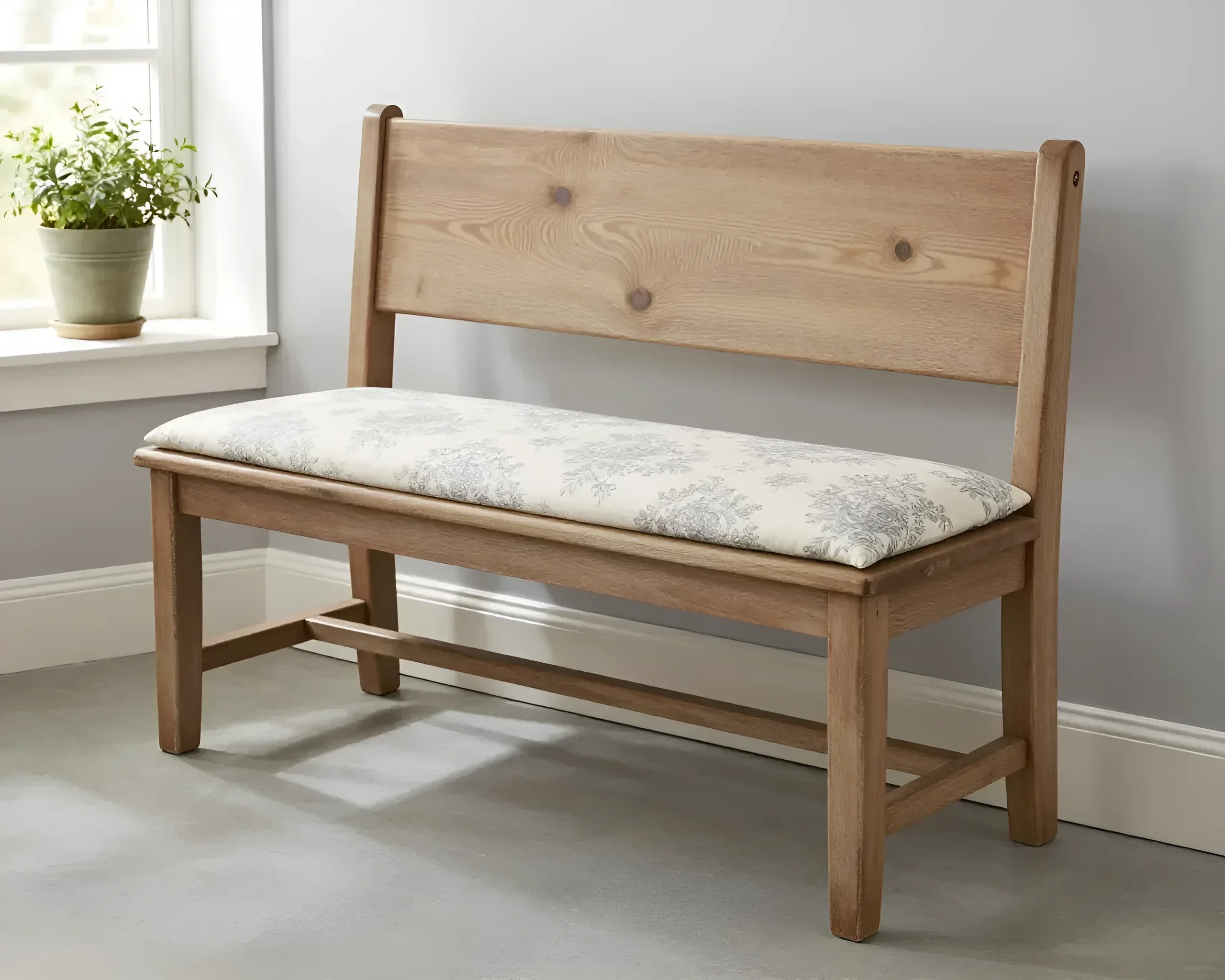 Светлая деревянная банкетка с подушкой в цветочный узор, расположенная у окна.