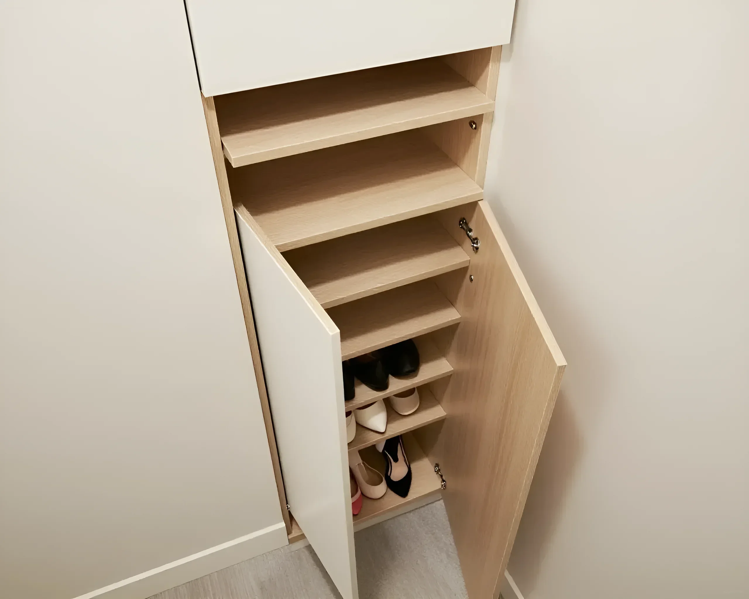 Schmaler Schuhschrank mit mehreren Regalen und einer Drehtür, der die ordentliche Aufbewahrung von Schuhen in einem kleinen Flur zeigt.