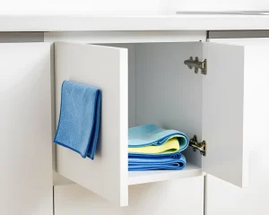 Белый кухонный шкаф с открытой дверцей, внутри сложены синие и желтые салфетки, на внешней стороне дверцы висит синяя салфетка.