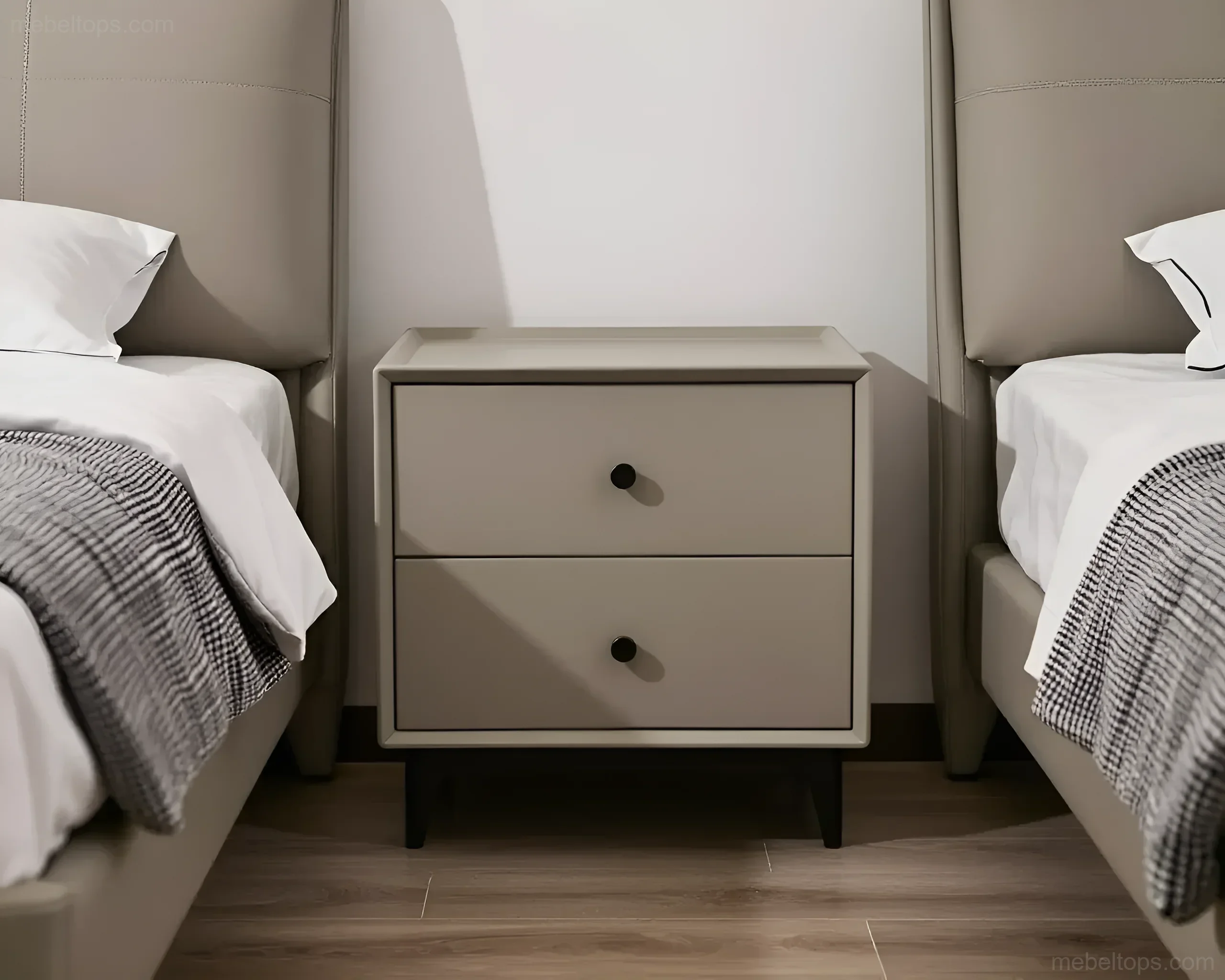 Minimalist gray bedside table with two drawers, placed between two beds with high headboards.