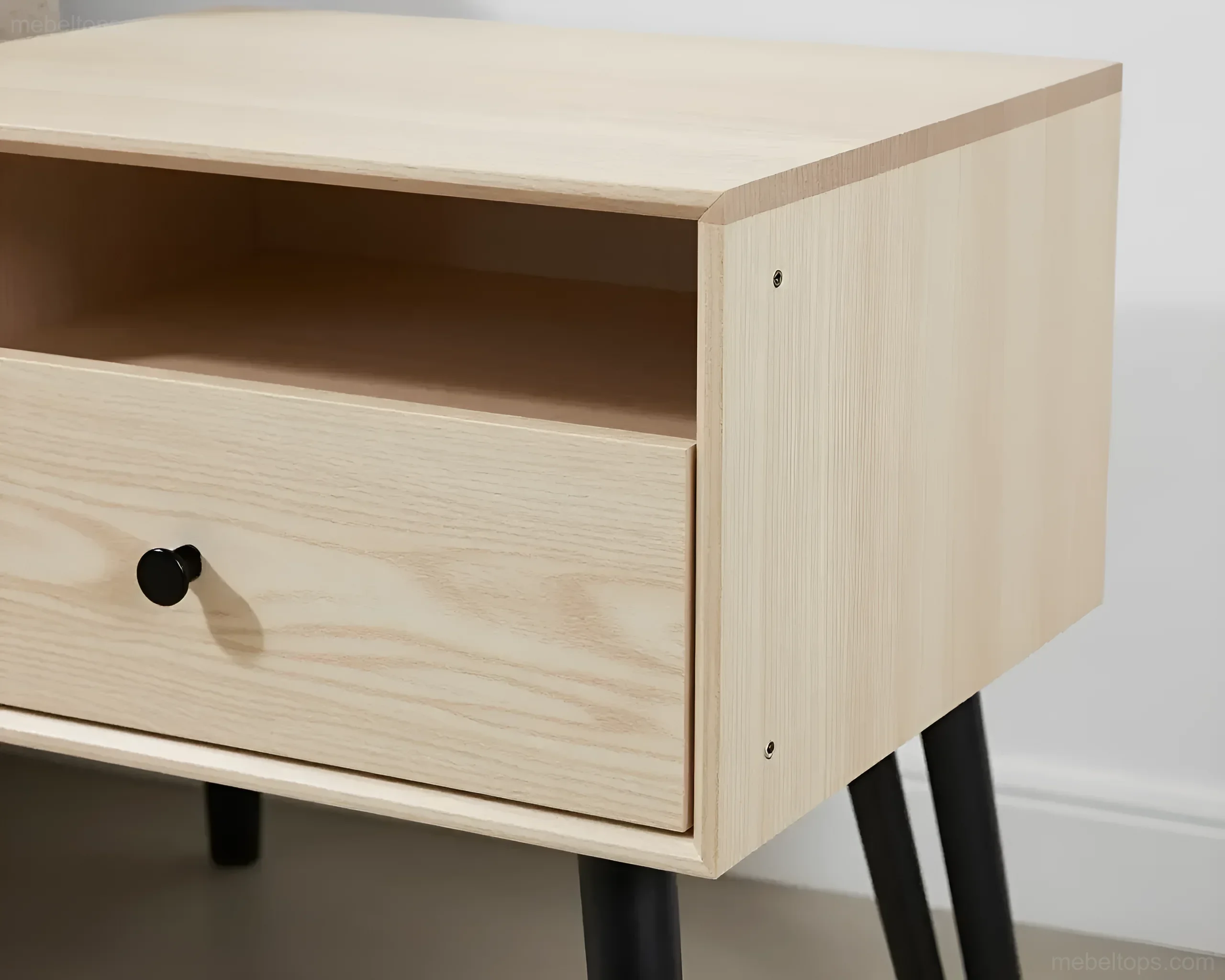 Light wooden bedside table with a black round drawer and open shelf, set on conical black legs.